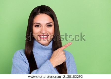 Photo of pretty sweet young woman wear blue sweater smiling pointing finger empty space isolated green color background