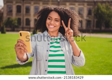 Photo of young cheerful african girl take picture cellphone show fingers peace cool v-symbol outdoors