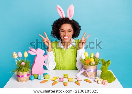 Photo of cool young brunette lady v-sign happy easter wear green vest isolated on blue color background