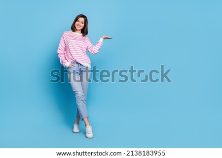 Full size photo of optimistic millennial lady stand hold promo wear shirt jeans shoes isolated on blue background