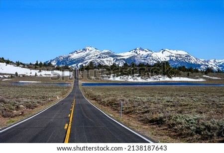 The road through the valley to the snow capped mountains. Mountain valley road landscape. Snowy mountain valley road way Royalty-Free Stock Photo #2138187643