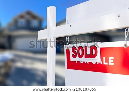 Red and white Sold sign in front of a house that is for sale and has recently been sold. Realtor sign outside of a sold house. 