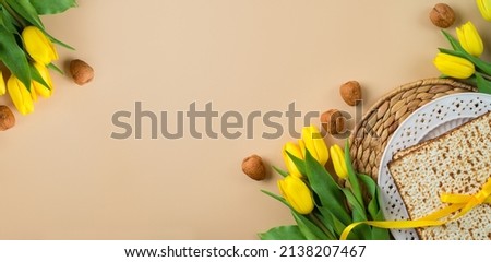 Jewish holiday Passover celebration concept with matzah, seder plate and yellow tulip flowers on modern background. Pesah top view frame border design with copy space Royalty-Free Stock Photo #2138207467