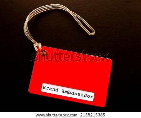 Red luggage tag with text BRAND AMBASSADOR, refer to person employed by organization or business owner to represent brand in positive image to increase brand awareness
