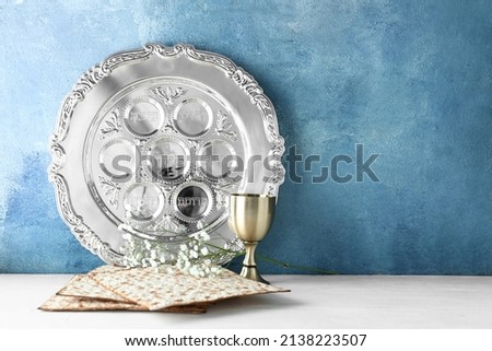 Passover Seder plate with cup of wine and matza on table against color background Royalty-Free Stock Photo #2138223507