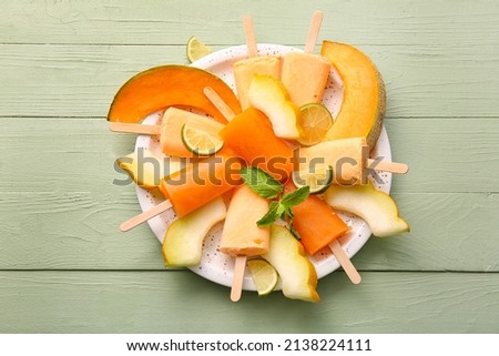 Plate with tasty popsicles and melon pieces on green wooden background