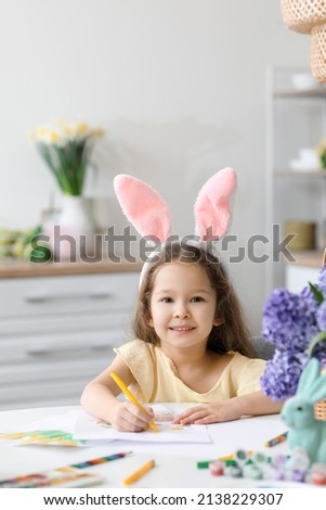 Cute little girl with bunny ears painting on Easter eve at home