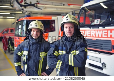 Group of firefighters at the emergency vehicle in the fire station  - sign at vehicle: Feuerwehr - Translation: fire department Royalty-Free Stock Photo #2138250045