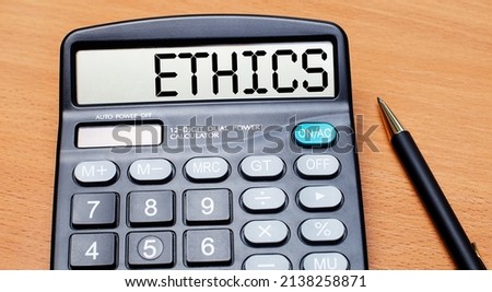 On a wooden table there is a black pen and a calculator with the text ETHICS. Business concept
