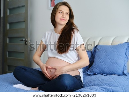 Young pregnant woman stroking big belly on couch
