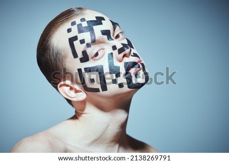 The concept of depersonalization and control over society. Portrait of a young man with a QR-code painted on his face, looking unfriendly directly at the camera. Studio portrait on a gray background. 