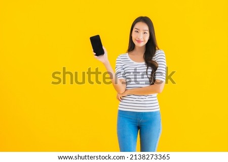 Portrait beautiful young asian woman smile happy use smart mobile phone on yellow isolated background