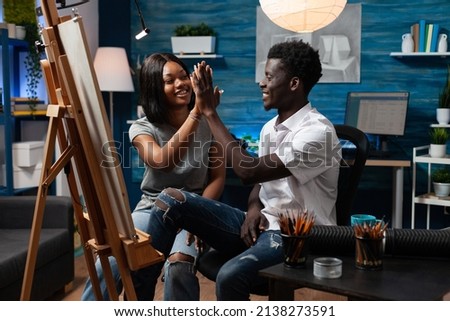 Young man artist giving high five to collegue after finished drawing vase illustration on canvas working with professional painting tools. Designer team sketching masterprice using graphic pencil