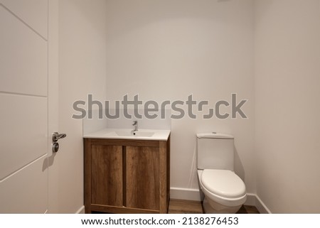 Bright modern powder room with white walls and sink unit with wooden doors, toilet and sink in brand new show home Royalty-Free Stock Photo #2138276453