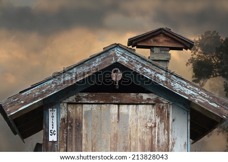 A vintage outhouse with a lock hanging from above.