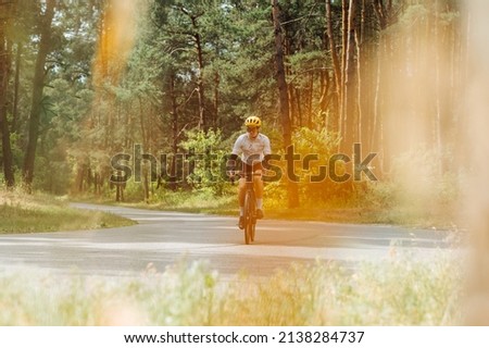 Male professional cyclist trains on a forest asphalt road. . Cycling in the woods. Professional cyclist trains outside the city, photo in orange tones
