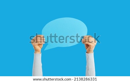 Unrecognizable woman holding empty blue speech bubble in hand on blue background. Blank paper card layout with copy space for message, quote, inspiration, opinion or vote. For advertisement