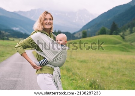 Babywearing. Mother and baby on nature outdoors. Baby in wrap carrier. Woman carrying little child in baby sling in green mint color. Concept of green parenting, natural motherhood, postpartum period. Royalty-Free Stock Photo #2138287233