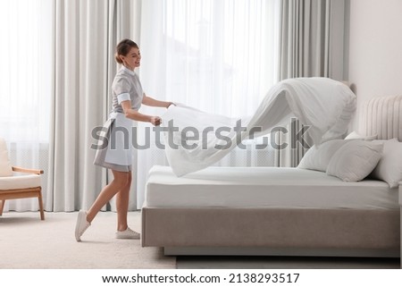 Professional chambermaid making bed in hotel room Royalty-Free Stock Photo #2138293517