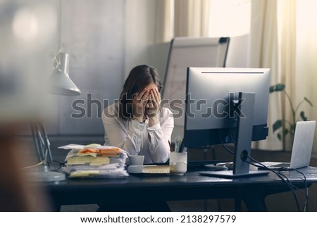 Very stressed business woman and female employee sitting in front of her computer with her hands in front of her eyes, feeling sad and depressed. Too much work - huge pile of paperwork at office table Royalty-Free Stock Photo #2138297579