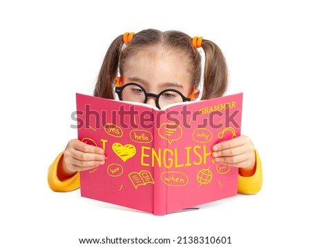 Beautiful cute little girl with glasses reading English grammar book in front of white background. Foreign language learning and speaking concept. I love English. Back to school. Royalty-Free Stock Photo #2138310601