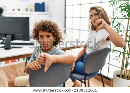 Young woman and son waiting at doctor appointment with angry face, negative sign showing dislike with thumbs down, rejection concept 