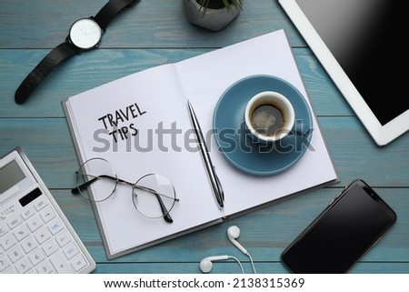 Notebook with phrase Travel Tips and office stationery on light blue wooden table, flat lay