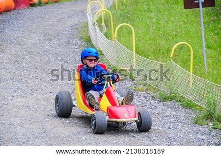 young boy rolling down hill in a go kart in the french alps at super devoluy ,holiday activity ,ski resort in summer .