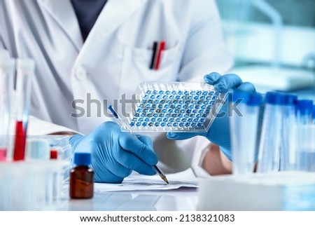 Researcher Sample Analysis and writes down the data result of for elisa analysis. Scientist working with samples panel microplate and registering data for diseases diagnostic in the laboratory Royalty-Free Stock Photo #2138321083