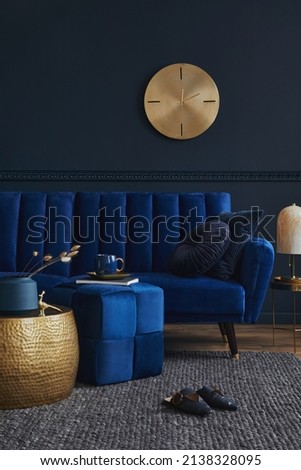 Elegant modern living room interior design with glamour blue velvet sofa, pouf, black metal shelf, poster, plants and modern home accessories. Dark blue wall. Template. Copy space. Royalty-Free Stock Photo #2138328095