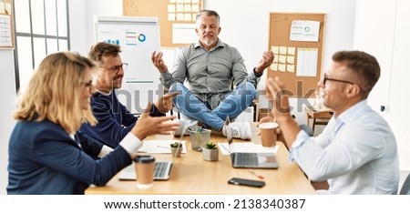 Businessman enjoys meditating during meeting. Sitting on desk near arguing partners at the office.