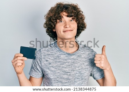 Handsome young man holding ssd memory smiling happy and positive, thumb up doing excellent and approval sign 