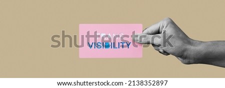 a person, in black and white, holds a sign with the text trans visibility cutout in it, with the colors of the transgender pride flag, on a beige background, in a panoramic format to use as web banner Royalty-Free Stock Photo #2138352897