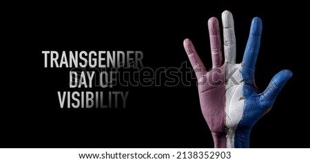 the raised hand of a person, with the transgender pride flag painted in it, and the text transgender day of visibility on a black background, in a panoramic format to use as web banner or header Royalty-Free Stock Photo #2138352903