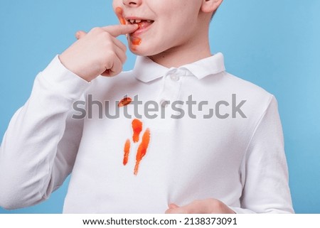 Close up stain tomato sauce spilling on white clothes. the child fingers tastes the tomato sauce. daily life stain concept.  Royalty-Free Stock Photo #2138373091