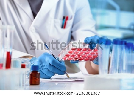 Scientist with Analysis to tissues and writes down the data result in the report. Researcher working with samples of tissue culture in microplate and registering data in the genetics laboratory Royalty-Free Stock Photo #2138381389