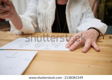 Focus on the hand of an unrecognizable fashion designer holding a pencil and drawing sketches for clothes, developing new line of dress collection