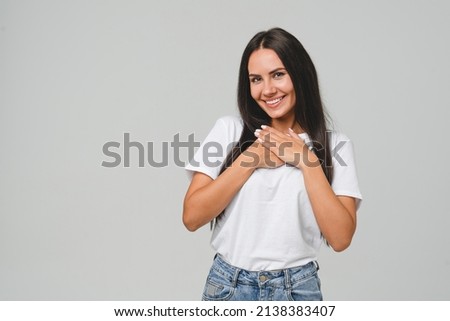 Touched pleased with a compliment cheerful happy caucasian young woman in white T-shirt isolated in grey background. Praise recommendation, sweet heart Royalty-Free Stock Photo #2138383407
