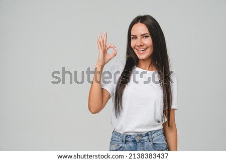 Positive caucasian young girl woman in white T-shirt showing okay gesture looking at camera, checking for good quality recommendation isolated in grey background. Well done! Great job!