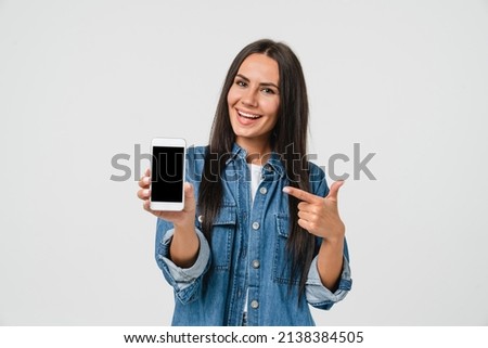 Excited young caucasian woman girl holding mobile phone pointing at cellphone blank screen with mockup copyspace, mobile application online, e-banking, social media networks isolated in white Royalty-Free Stock Photo #2138384505