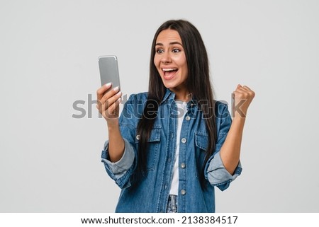 Extremely happy as a winner caucasian young woman celebrating victory in bets online casino lottery with money fortune using smart phone cellphone isolated in white background
