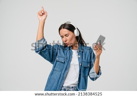 Energetic caucasian young woman girl dancing singing listening to the music podcast song singer sound track e-book in headphones earphones on cellphone isolated in white background Royalty-Free Stock Photo #2138384525