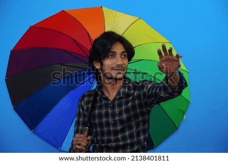 Young handsome man holding colorful umbrella and giving amazed expression, fear and excited face.