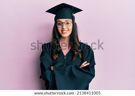 Young hispanic woman wearing graduation cap and ceremony robe happy face smiling with crossed arms looking at the camera. positive person.  Royalty-Free Stock Photo #2138411005