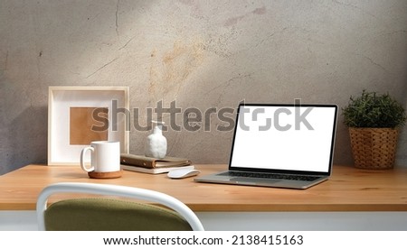 Computer laptop with empty screen, coffee cup, picture frame and potted plant on wooden table. Home office.