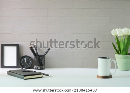 Stylish workplace with empty picture frame, coffee cup, notebook and tulips in a pot. Copy space for advertise text or information content.