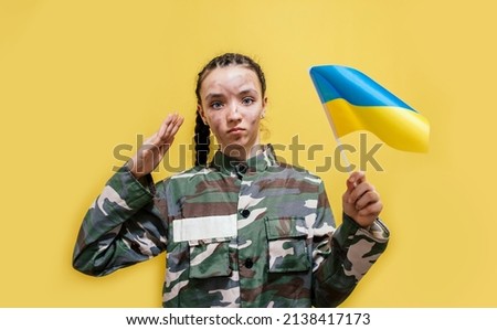 Ukrainian girl kid in military uniform with a dirty face, salutes. Child against war