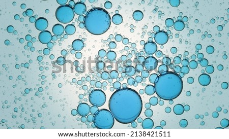 Blue different sized drops of oil floating in clear fluid on cyan background | Macro shot of emolient ingredients for its commercial