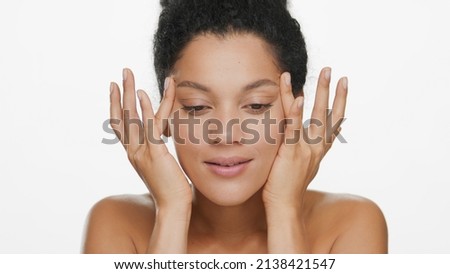 Close-up beauty portrait of slim African American young woman with gently touches her face with fingertips lifting skin around eyes on white background | Droopy eyes removal concept Royalty-Free Stock Photo #2138421547