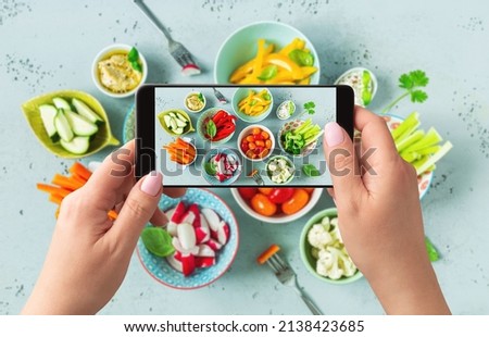 Food blogger taking photo of fresh, raw, sliced vegetables in the colorful bowls with smartphone. Lifestyle trend - posting and sharing food pictures on social media.